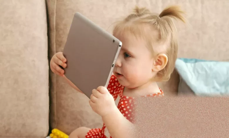 A baby lying on a play mat next to a smartphone on the floor.