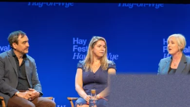 A silent author sitting on stage at the Hay Festival while the audience watches