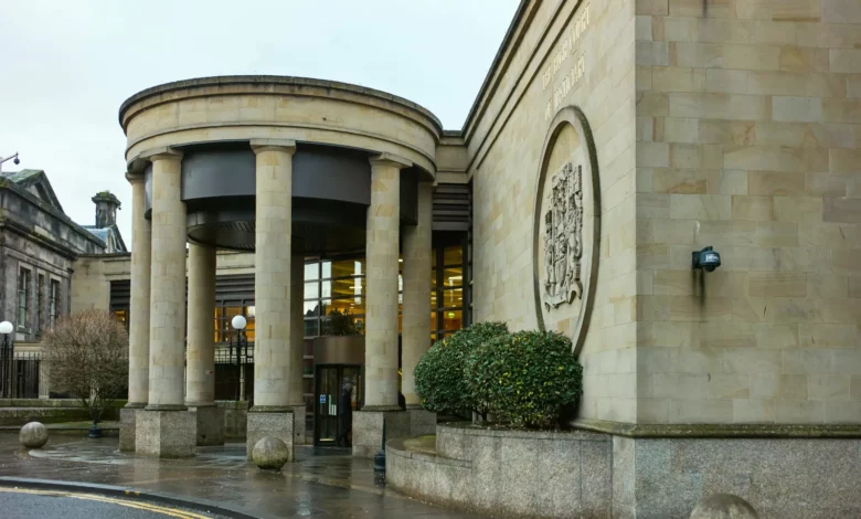A courtroom interior with a judge's bench and legal desks, setting for a Glasgow High Court trial