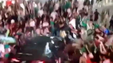 A black car surrounded by a crowd of Mexico fans in green shirts on a boulevard at night