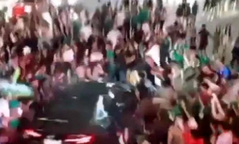A black car surrounded by a crowd of Mexico fans in green shirts on a boulevard at night