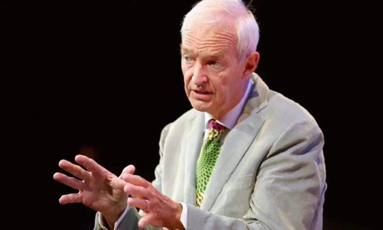 An older man speaking on a television news set with studio lights and cameras