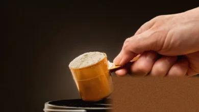 Whey protein powder being scooped from a large container in a UK warehouse