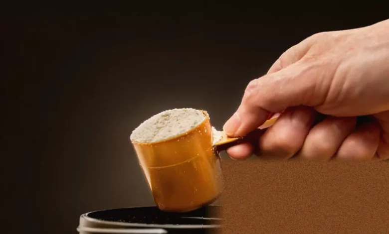 Whey protein powder being scooped from a large container in a UK warehouse