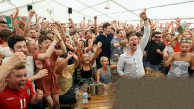 A crowded pub interior with patrons watching a football match on large screens late at night