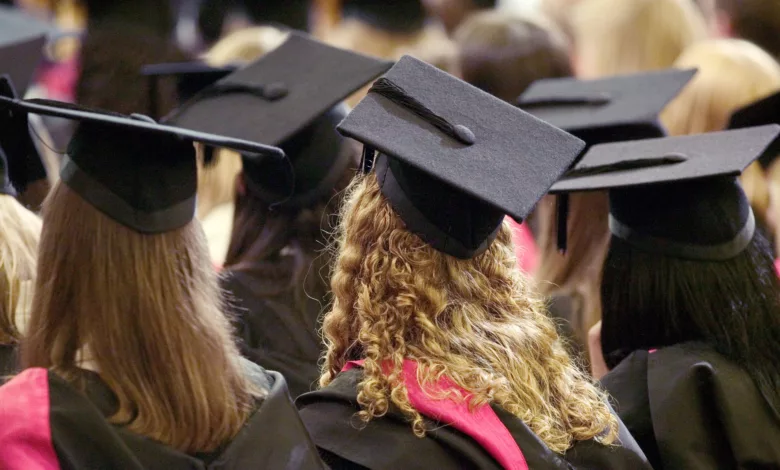 A university graduation ceremony in a UK campus hall, with graduates in caps and gowns.