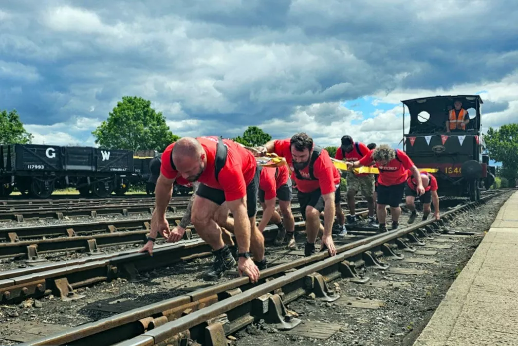 Spectators watching from a platform as a team manually hauls a heavy steam engine on rails